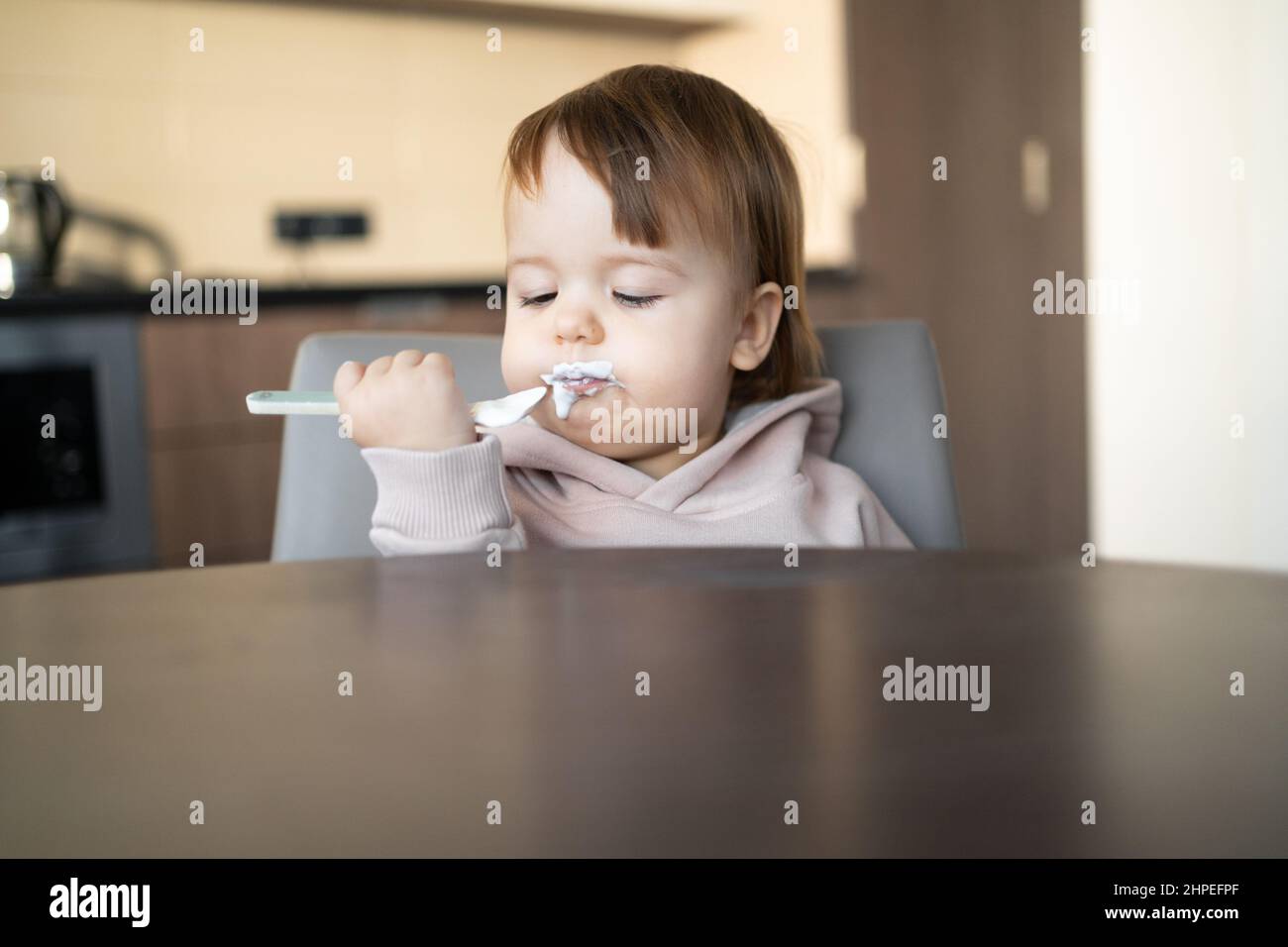Une Fillette Heureuse S Assoit A La Table Tient Une Cuillere Dans Ses Mains Et Mange Du Yaourt Un Bebe Sale Lui Meme A Le Petit Dejeuner A La Maison Avec Un Produit Laitier