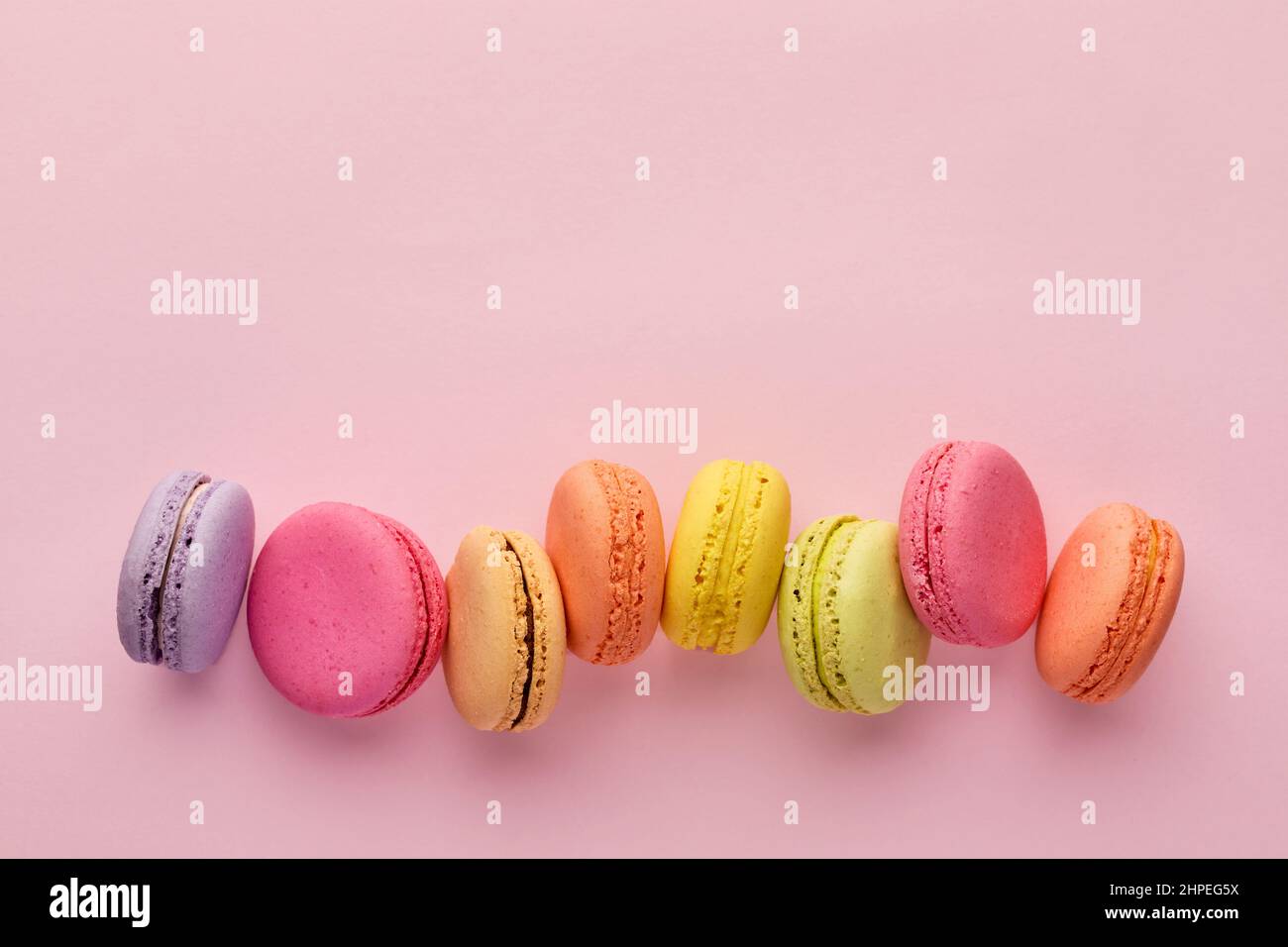Délicieux dessert français coloré macaron ou macarons dans une rangée sur fond rose. Vue de dessus avec espace de copie. Banque D'Images