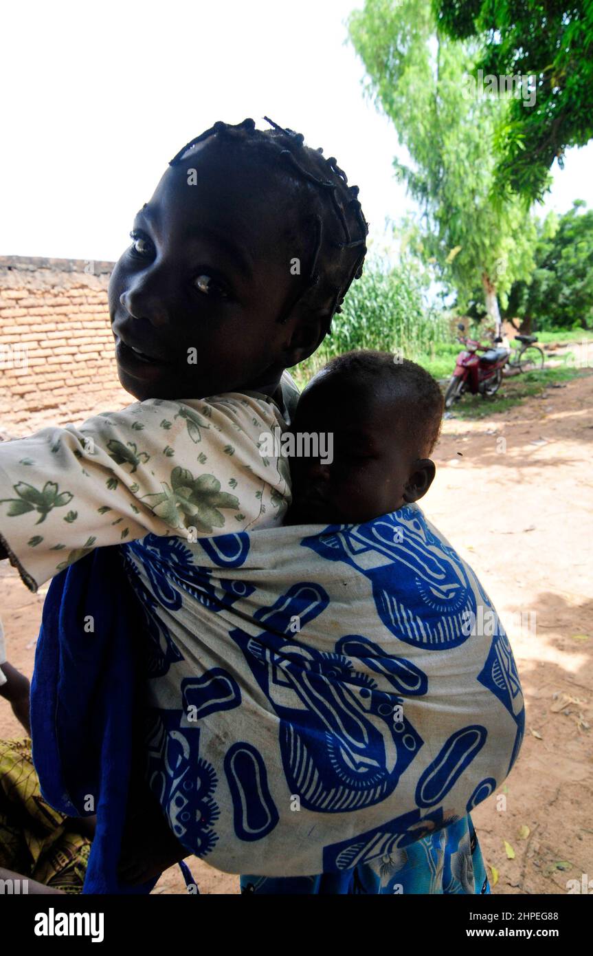 Une fille burkinabe portant son petit frère sur le dos. Centre du Burkina Faso. Banque D'Images