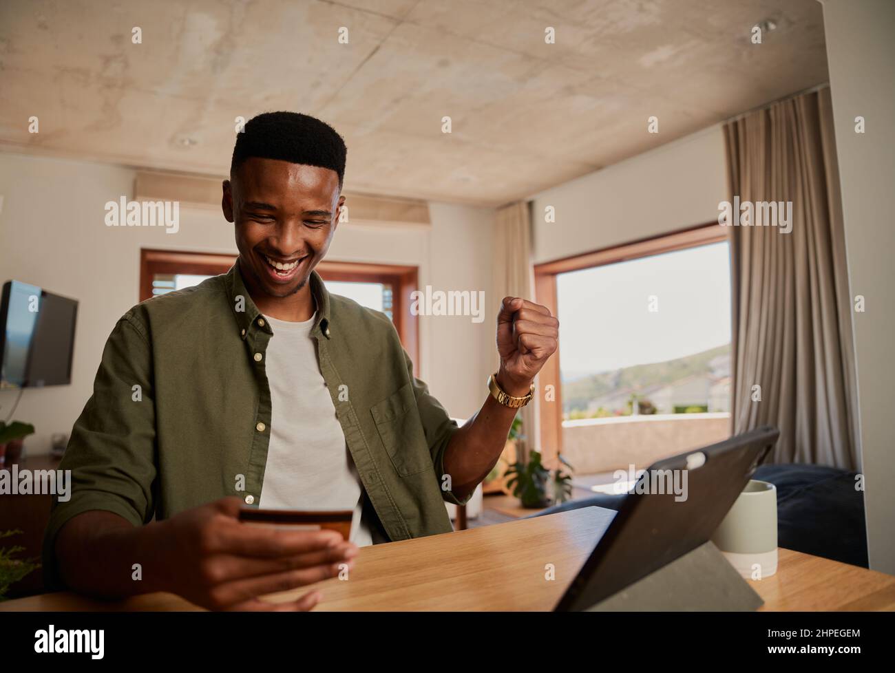 Joyeux jeune adulte noir homme utilisant la tablette électronique, célébrant au sujet de faire l'achat en ligne à la maison. Banque D'Images