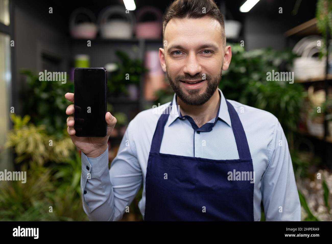 un vendeur de fleurs sur fond de fleuriste montre un écran de smartphone avec un sourire sur son visage Banque D'Images