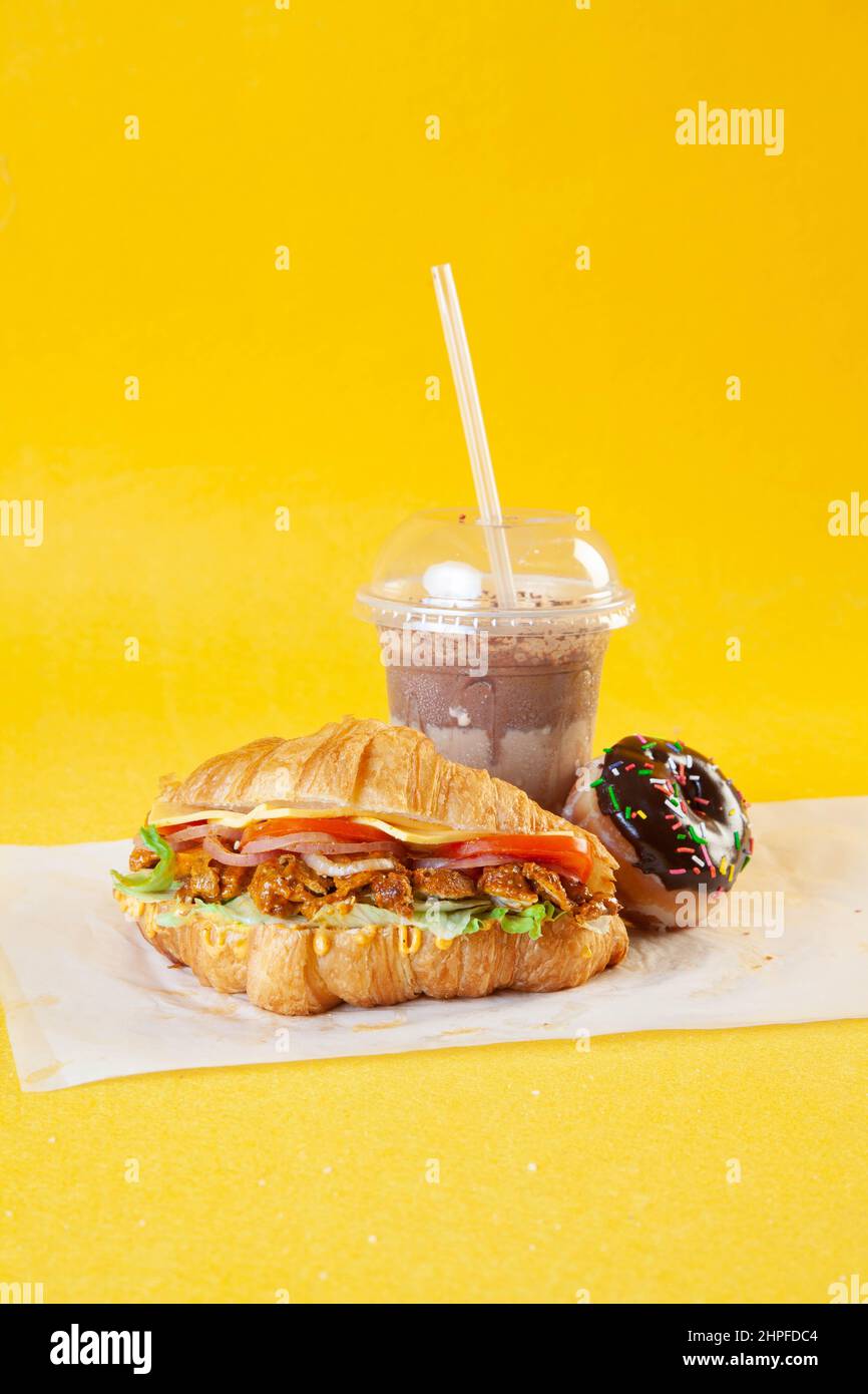Sandwich croissant brioche avec tranches de poulet tikka épicées, tomates et fromage avec beignet et café froid Banque D'Images