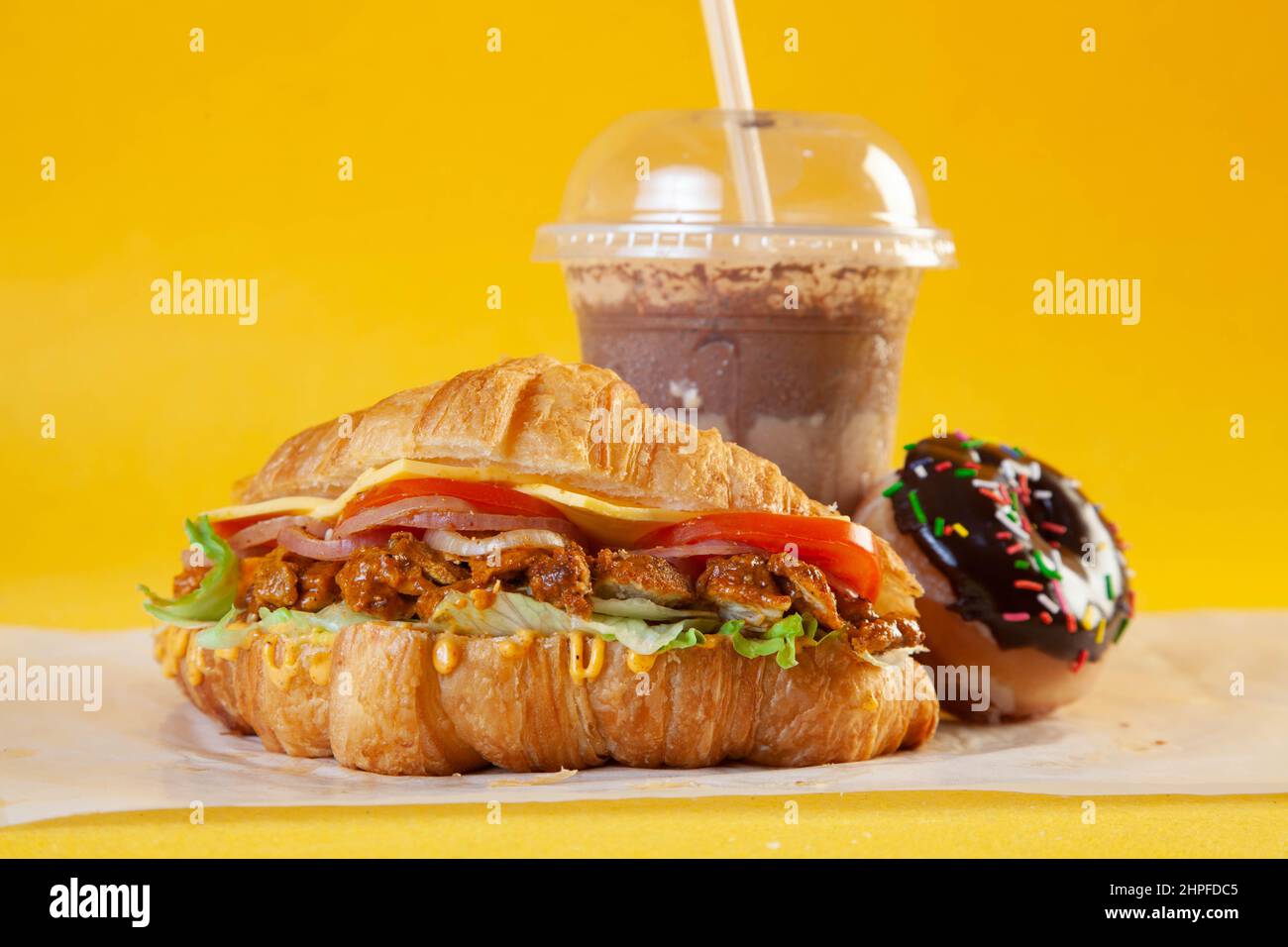 Sandwich croissant brioche avec tranches de poulet tikka épicées, tomates et fromage avec beignet et café froid Banque D'Images