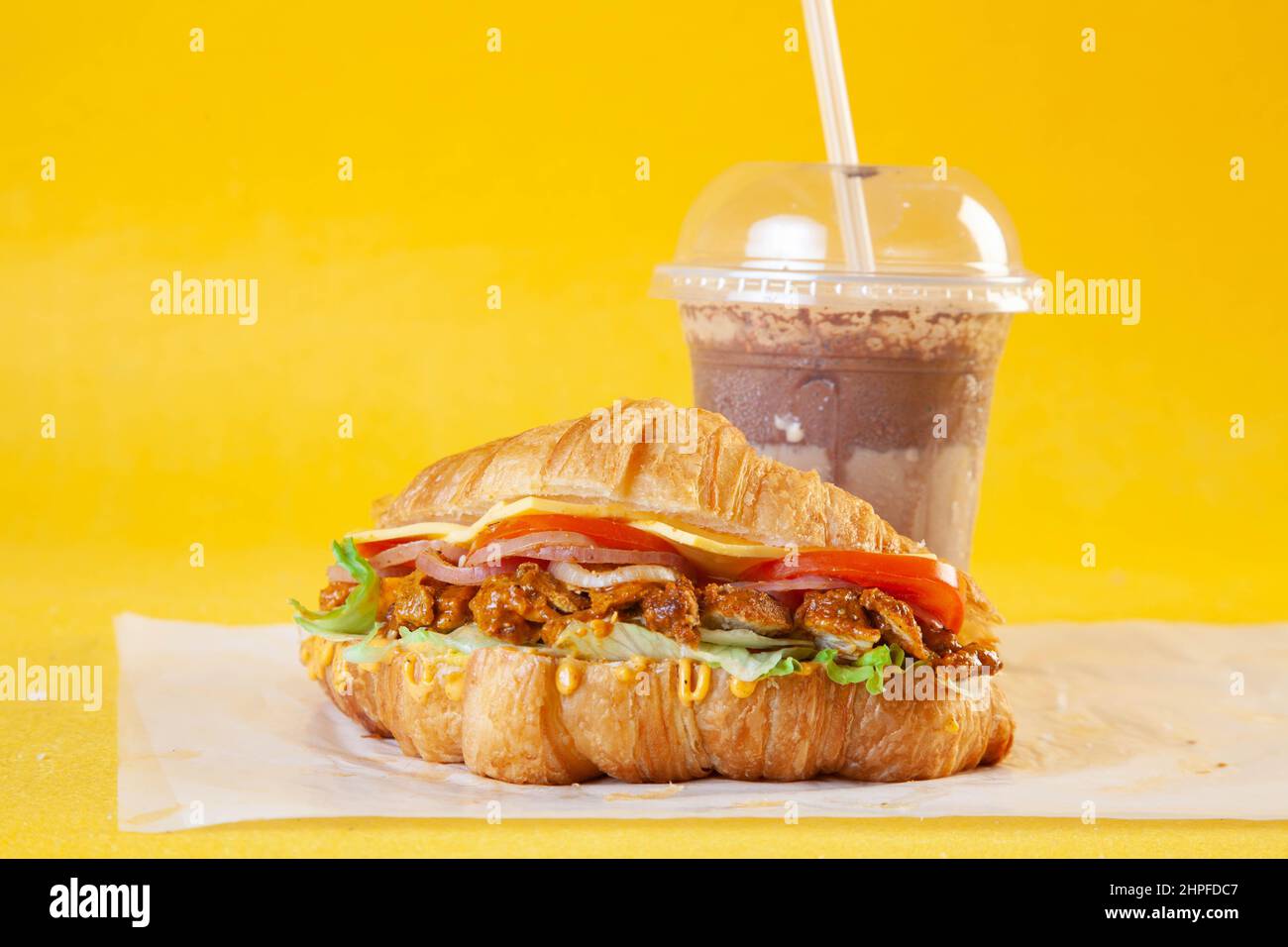 Sandwich croissant brioche avec tranches de poulet tikka épicées, tomates et fromage avec beignet et café froid Banque D'Images
