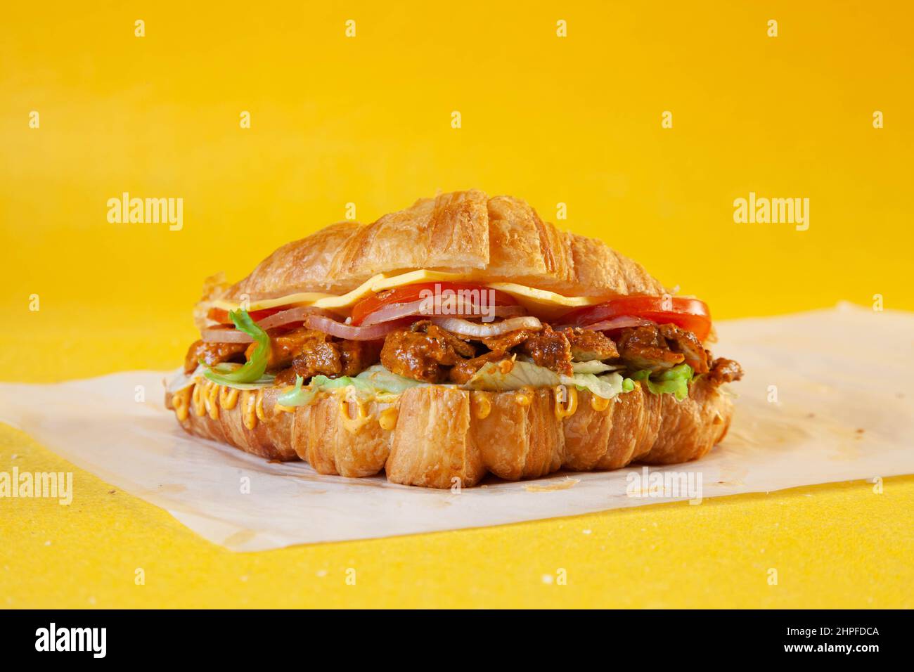 Sandwich croissant brioche avec tranches de tikka de poulet épicées, tomates et fromage. Banque D'Images