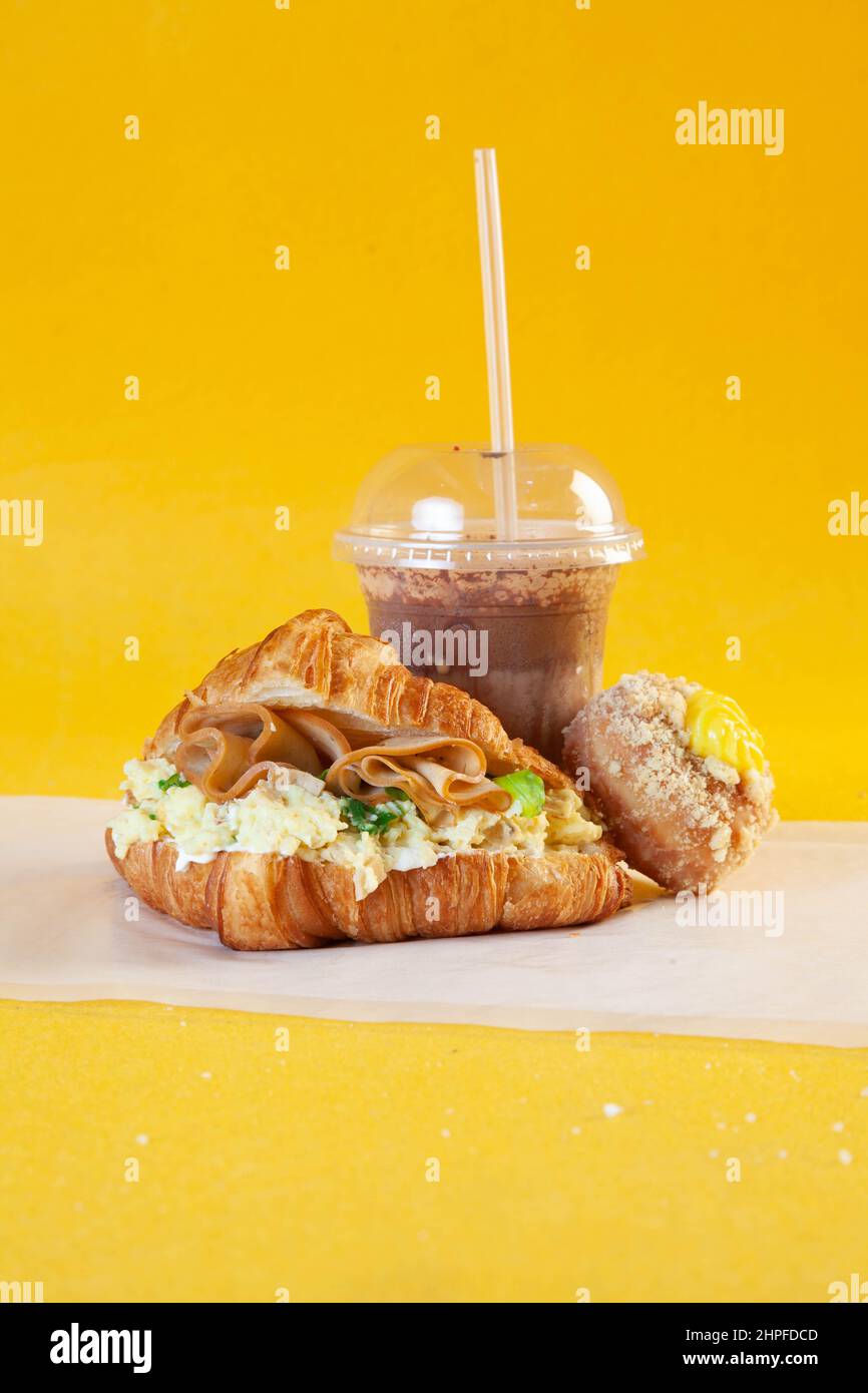 Sandwich aux œufs brouillés écrosé avec café froid et beignet. Banque D'Images