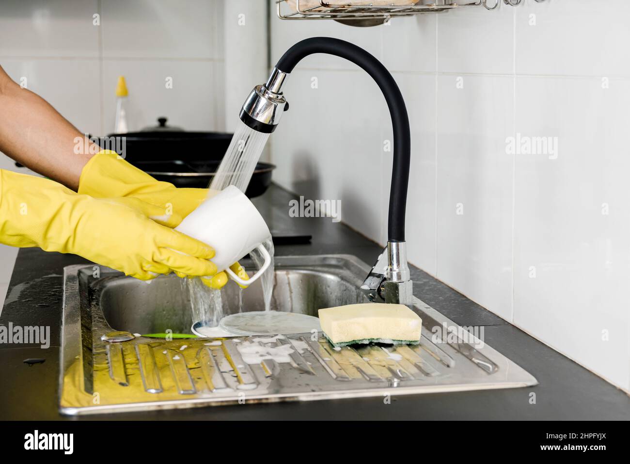 Fermez les mains humaines dans des gants en caoutchouc jaune en lavant une tasse de café en céramique dans l'évier de cuisine. Banque D'Images Fermez les mains humaines dans des gants en caoutchouc jaune en lavant une tasse de café en céramique dans l'évier de cuisine. Banque D'Images