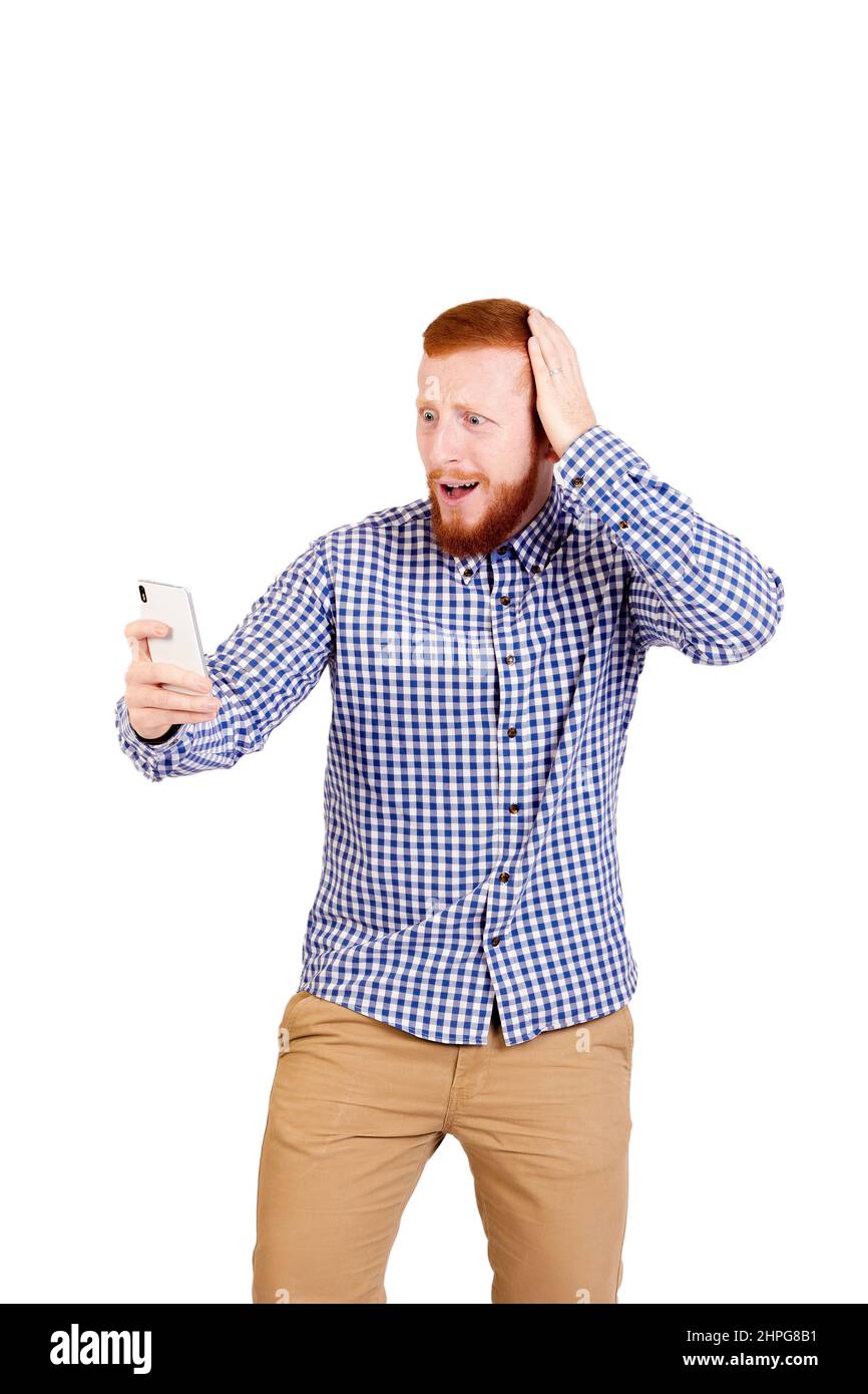 Un homme confus aux cheveux rouges dans une chemise élégante et décontractée regardant l'écran de smartphone, un gars est en train de lire les mauvaises nouvelles, le choc et la déception homme regarde le téléphone avec le visage embarrassé. Photo de haute qualité Banque D'Images