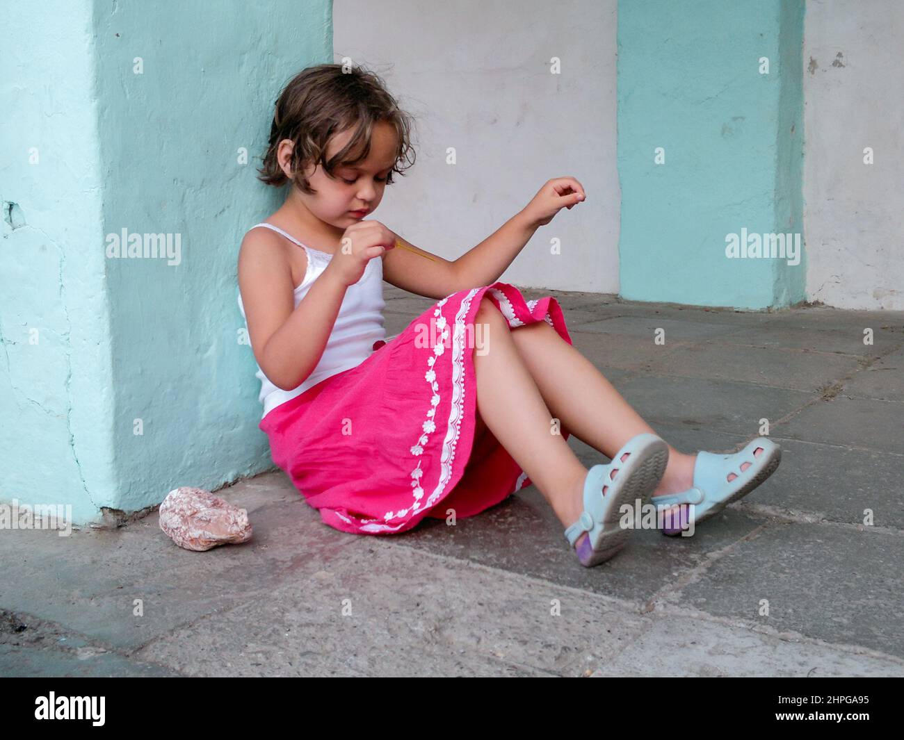 Jolie fille est assise sur le sol en pierre et joue. Le concept de comportement de l'enfant. Copier l'espace. Banque D'Images