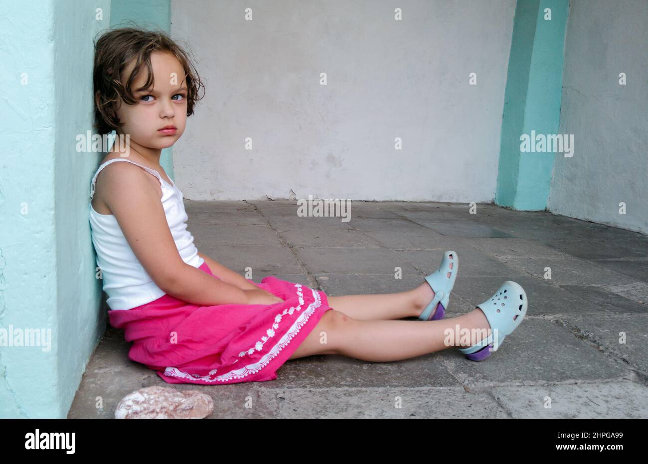Mignonne fille en colère est assise sur le sol, regardant l'appareil photo. Concept de problème de comportement des enfants. Banque D'Images