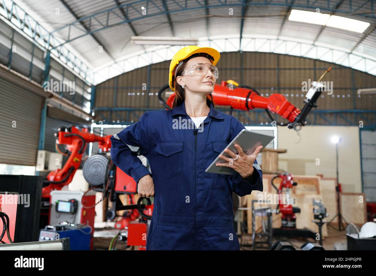 Jeune femme professionnelle d'usine industrielle travaillant avec des pièces de machines à mettre, vérifier et tester des équipements industriels et des bras robotisés dans Banque D'Images