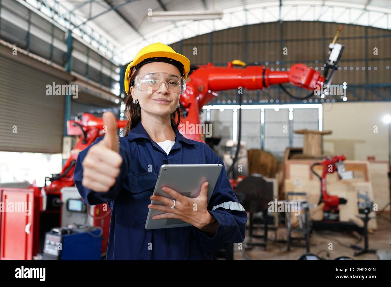 Jeune femme professionnelle d'usine industrielle travaillant avec des pièces de machines à mettre, vérifier et tester des équipements industriels et des bras robotisés dans Banque D'Images