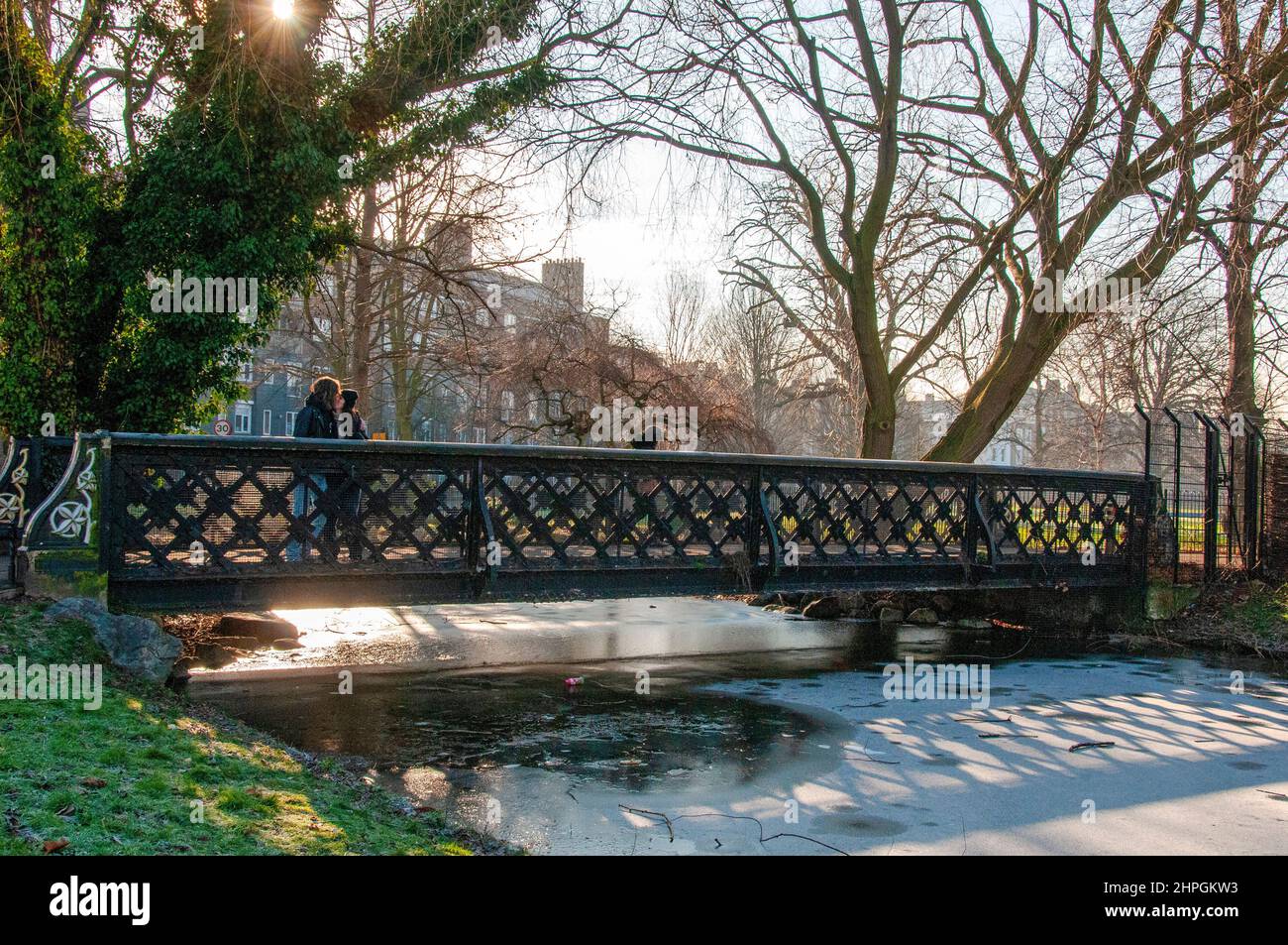 Personnes traversant le pont au-dessus de la rivière New sous un soleil hivernal brumeux, Clissold Park, Stoke Newington, London Borough of Hackney Banque D'Images