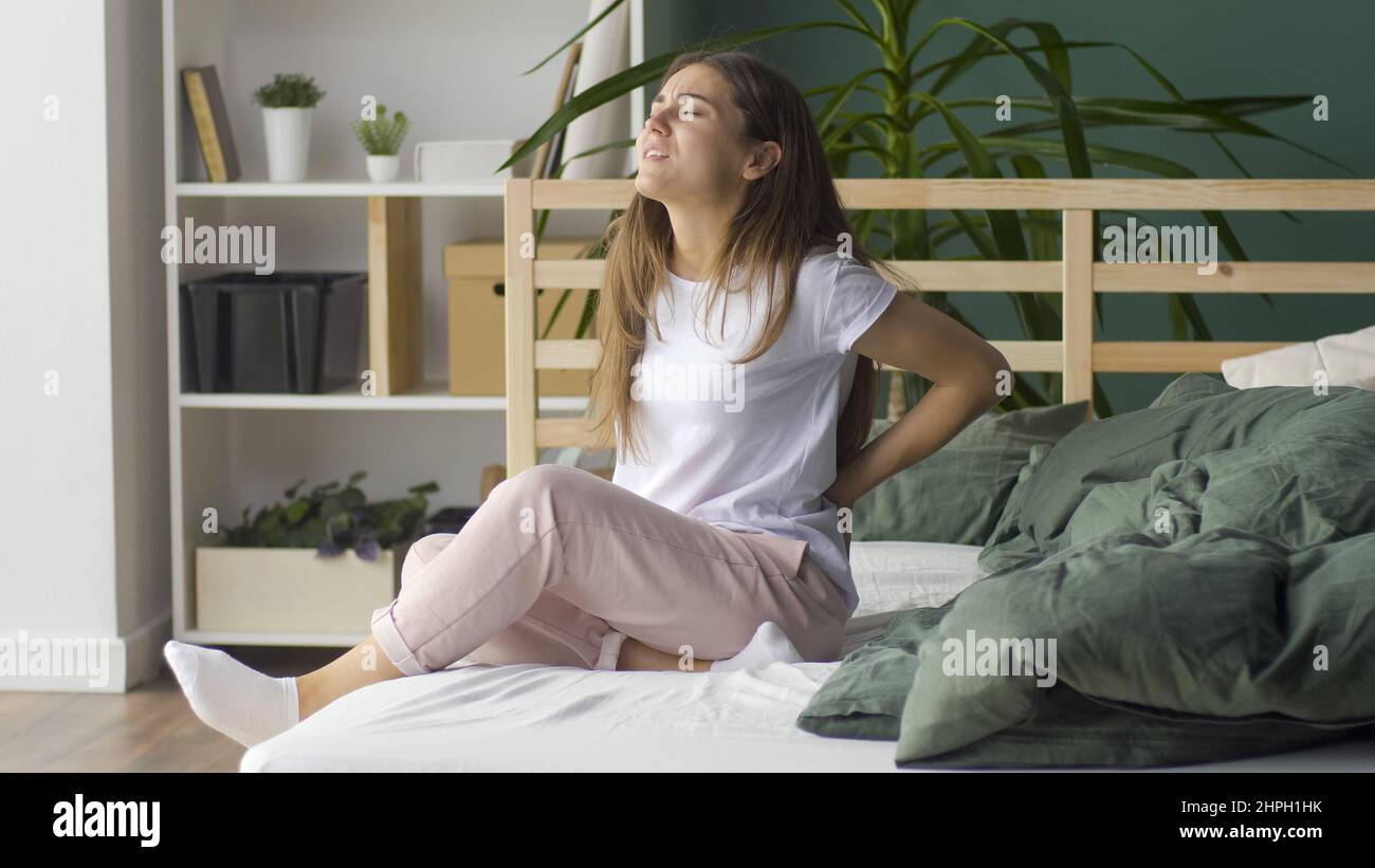 La jeune femme ressent des douleurs au dos sur le lit à la maison, frotte son dos inférieur, mal de sommeil Banque D'Images