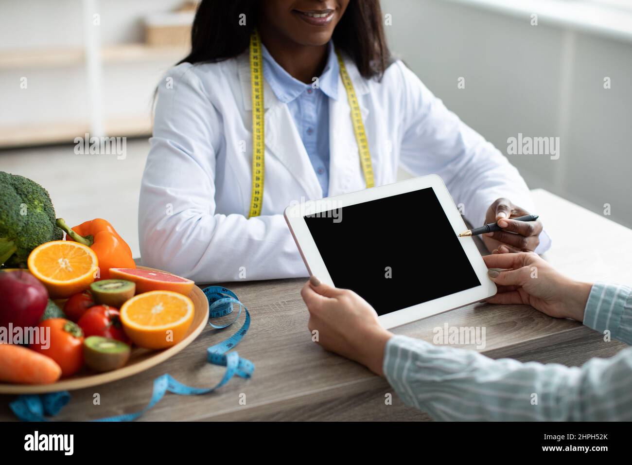 Diététiste féminine noire pointant sur un comprimé avec écran blanc, expliquant le plan de régime et donnant des conseils au patient Banque D'Images
