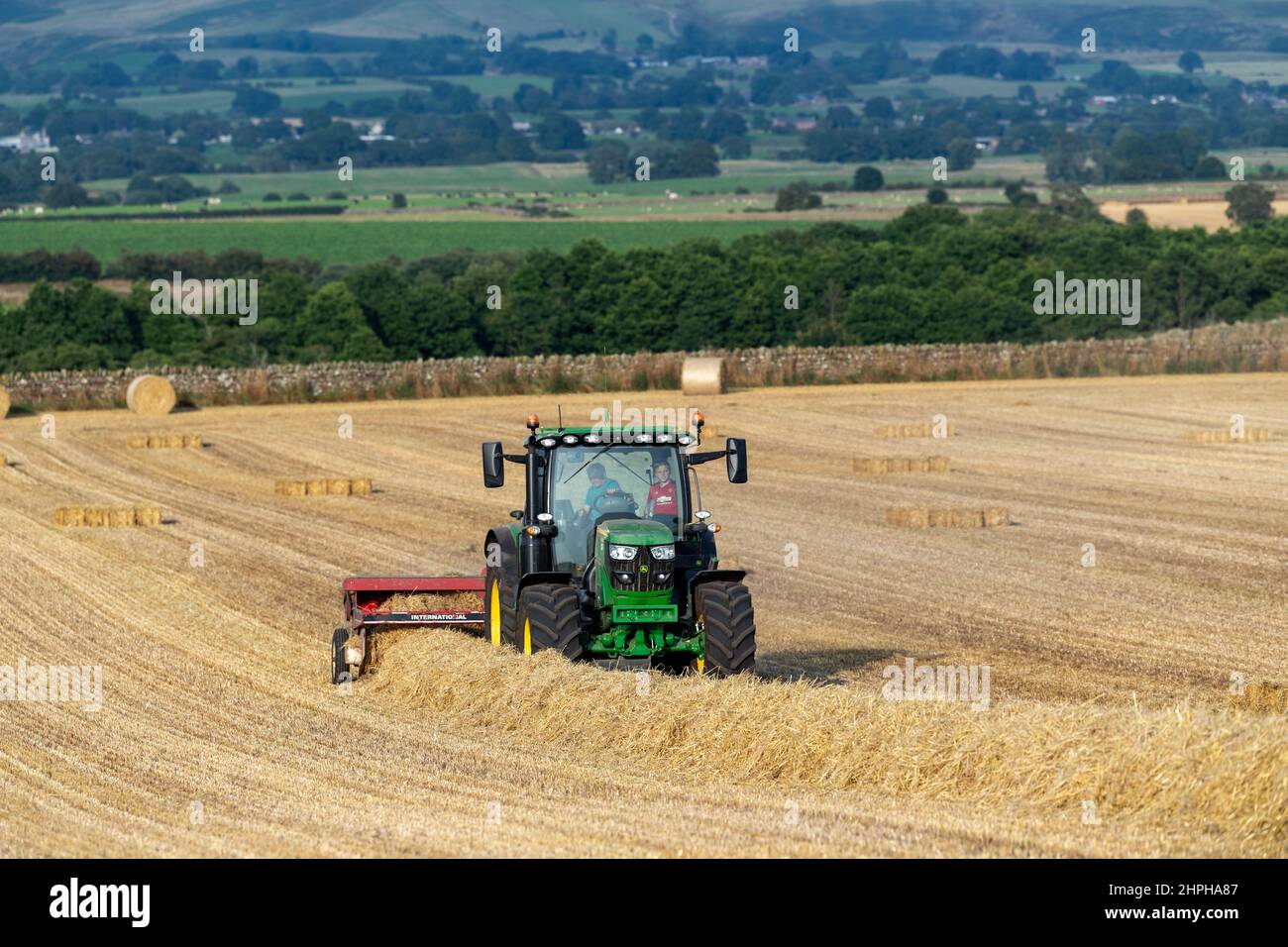 Réalisation de balles de paille pour la litière d'animaux avec un tracteur John Deere 6130R et une ancienne presse internationale et un système plat 8. Eden Valley, Cumbria, Royaume-Uni. Banque D'Images