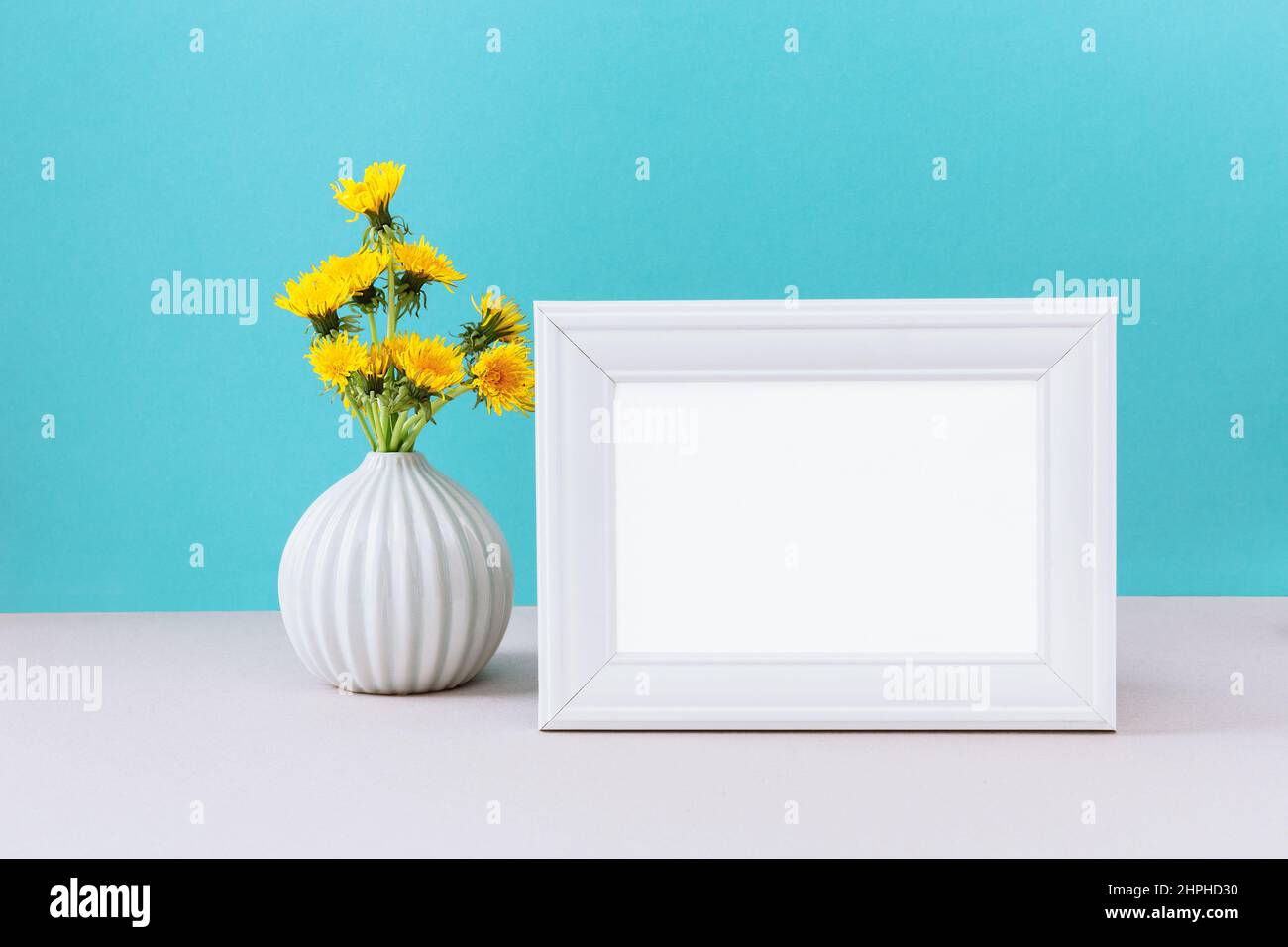 Maquette de cadre blanc avec fleurs de pissenlit jaune sauvage dans un vase. Maquette avec cadre vide pour un motif de présentation. Modèle blanc sur fond cian Banque D'Images