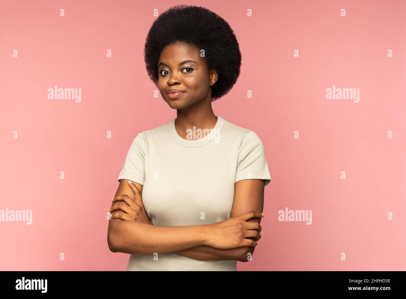 Femme noire étudiante souriante avec des mains croisées pensant regarder la caméra sur le mur rose studio Banque D'Images
