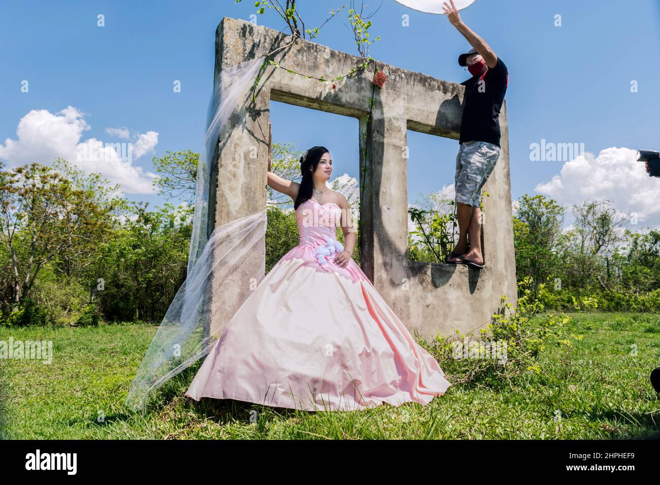 Une jeune fille cubaine de quinze ans pose pour une photo à l'extérieur à midi portant une vieille robe large longue mode. Il y a un jeune homme qui tient un diff fait maison Banque D'Images