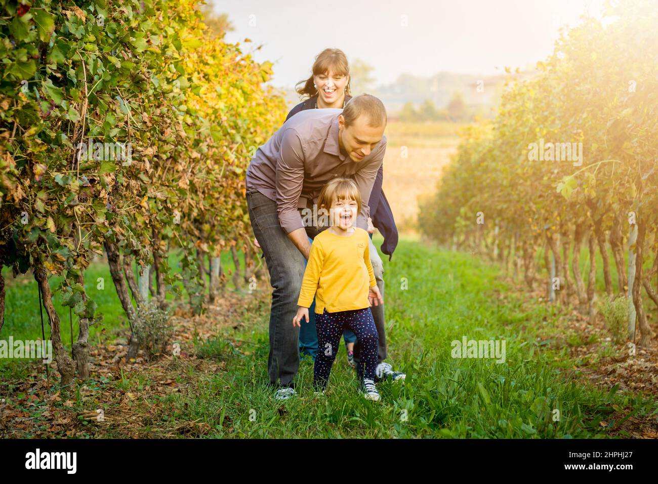 Belle jeune famille souriante de trois personnes s'amusant, plaisantant et marchant ensemble dans un vignoble Banque D'Images
