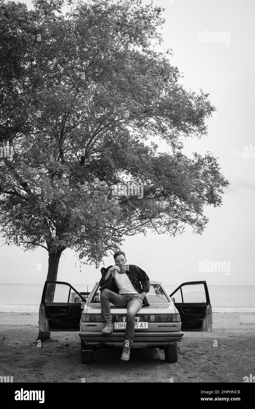 beau homme dans les lunettes près de la voiture et de l'arbre noir et blanc Banque D'Images
