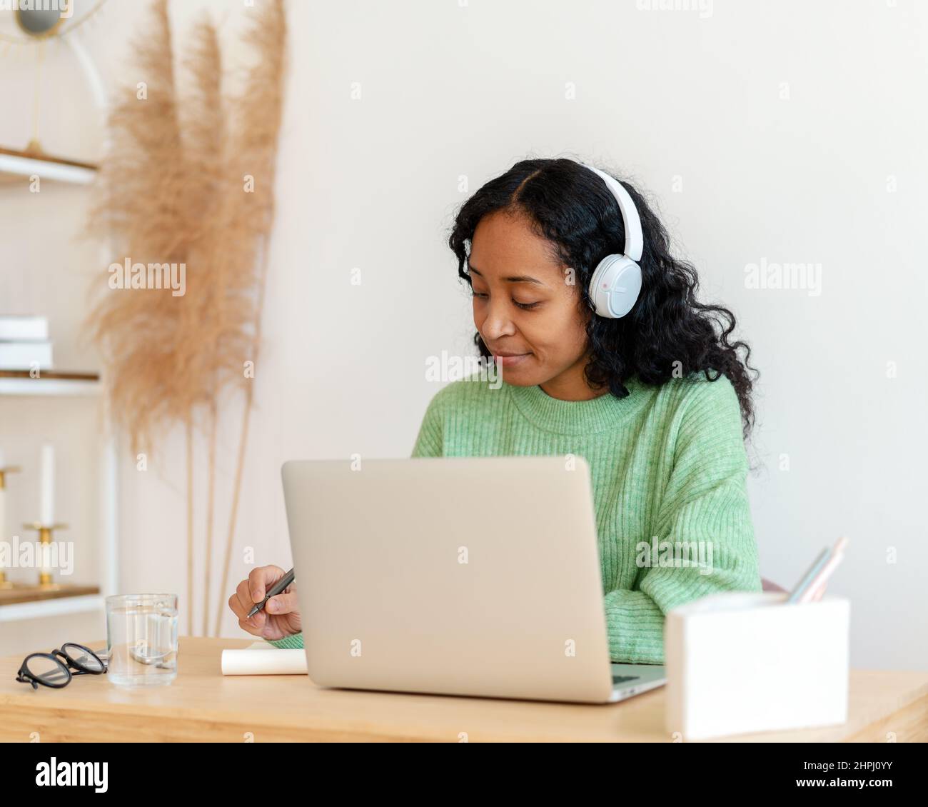 Une femme afro-américaine prend des notes tout en écoutant un podcast audio dans un casque. Cours en ligne Banque D'Images