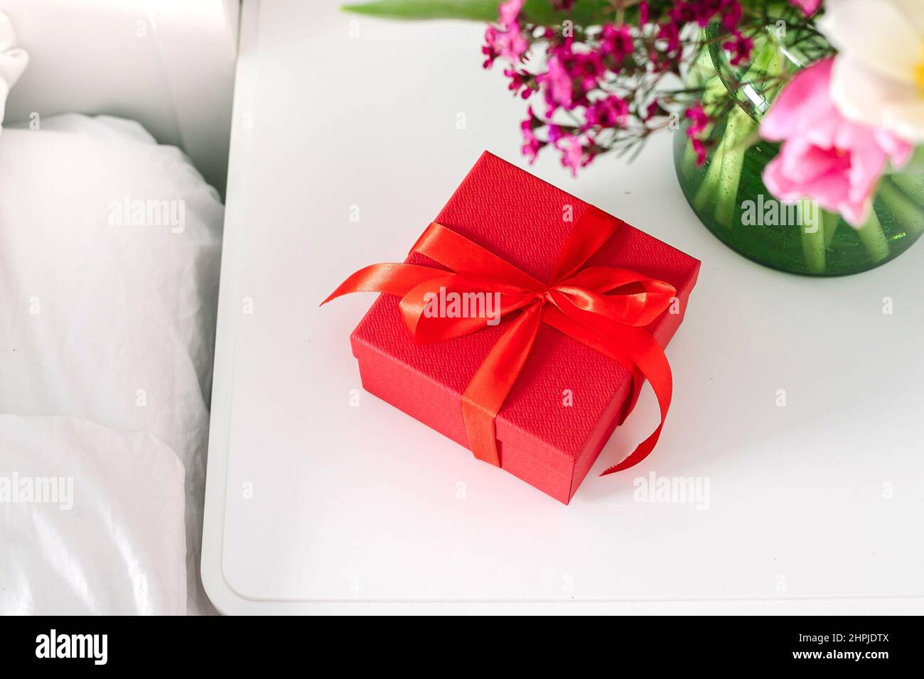 Bouquet de tulipes et boîte cadeau rouge sur la table de nuit près du lit dans la chambre. Concept du jour des femmes, jour des mères Banque D'Images