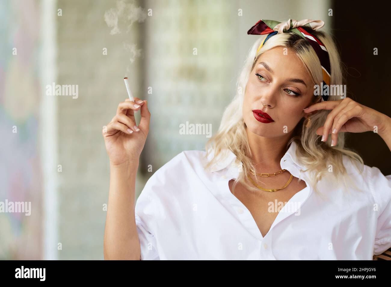 Portrait d'une jeune femme aux yeux verts, portant un foulard et une chemise blanche, tout en fumant de la cigarette. Banque D'Images