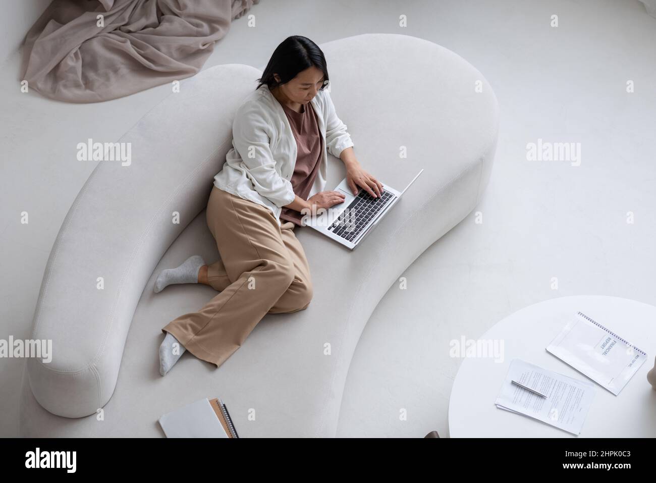 Jeune femme sérieuse avec un ordinateur portable allongé sur un canapé tout en réseau, en faisant des achats en ligne ou en travaillant avec des données financières à la maison Banque D'Images