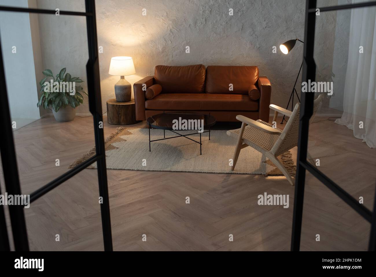 Grande chambre de luxueux appartement avec canapé en cuir debout par mur au centre entouré d'une petite table, fauteuil, deux lampes et plante verte Banque D'Images
