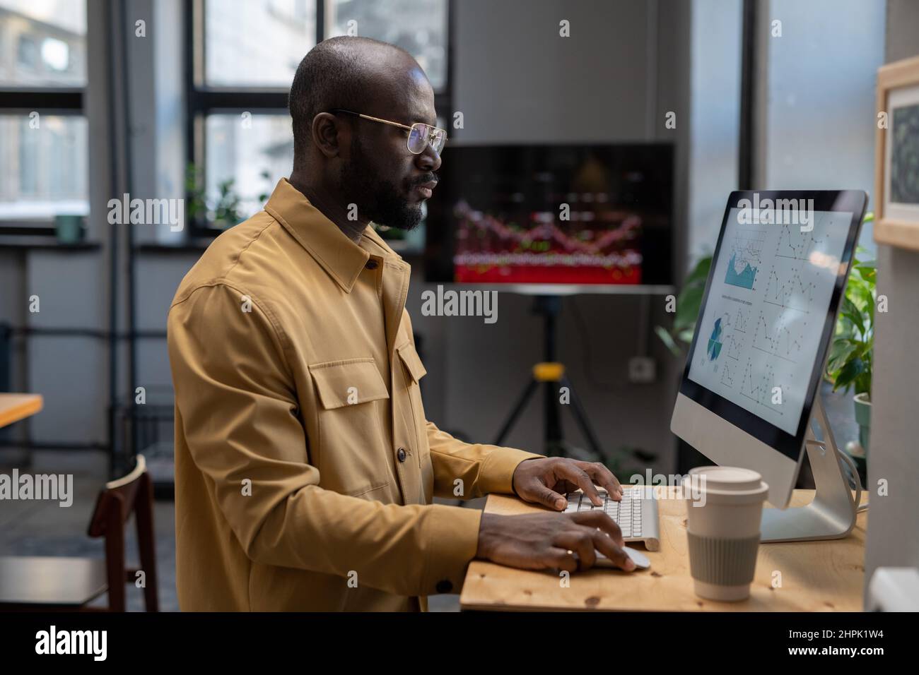 Jeune économiste sérieux contemporain analysant des diagrammes et des graphiques à la finition sur écran d'ordinateur tout en étant assis sur le lieu de travail au bureau Banque D'Images