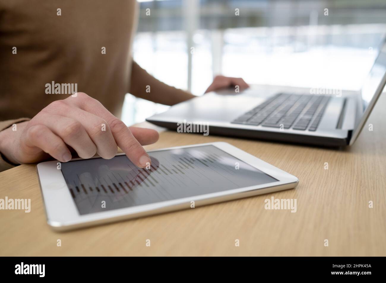 Main de jeune homme d'affaires pointant sur les données sur l'écran d'une tablette tout en analysant les graphiques pendant le travail sur les nouveaux projets d'affaires par table Banque D'Images