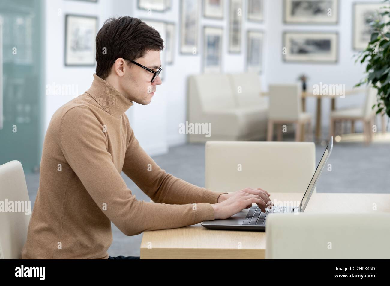 Vue latérale d'un jeune développeur sérieux de la société de technologie tapant sur le clavier d'ordinateur portable tout en étant assis près du lieu de travail dans un bureau moderne Banque D'Images