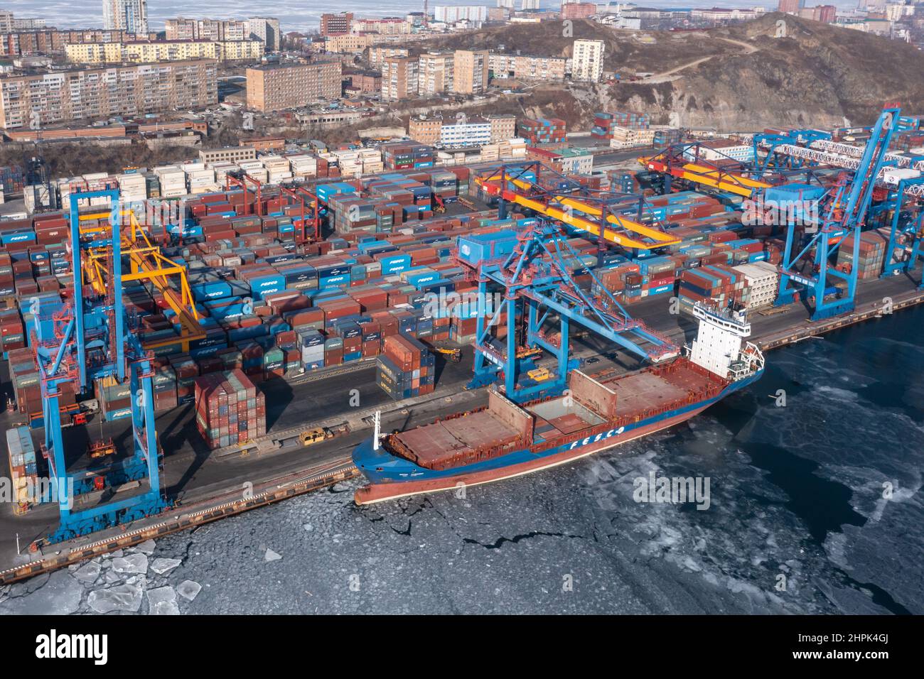 Vladivostok, Russie - 27 janvier 2022 : Vue de dessus du terminal des conteneurs du port maritime et de la ville.En hiver, un bateau à conteneurs est en train de charger au quai. Banque D'Images