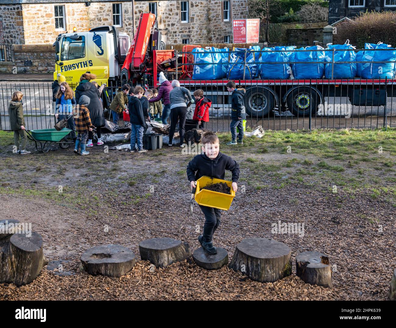 Trinity Primary School, Édimbourg, Écosse, Royaume-Uni, 22 février 2022. Terre végétale pour les écoles : excavation pendant le projet de biomes du jardin botanique royal, un surplus de terre végétale de 50 tonnes est accordé aux écoles, aux allotissements et aux organismes communautaires par la société de construction Balfour Beatty. Une livraison de 5 tonnes a lieu à l'école primaire Trinity pour transporter la terre ou la terre pour remplir les planteurs dans le jardin de l'école pour que les élèves cultivent des légumes. Les élèves du primaire 4 utilisent des récipients de toutes formes et tailles pour déplacer la terre pour remplir les planteurs ; un travail d'équipe est nécessaire Banque D'Images
