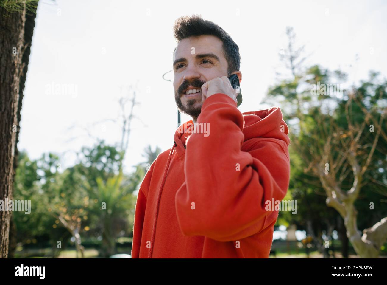 Un téléphone parlant, un jeune homme heureux regardant de côté tout en parlant par son téléphone. Beau homme en train de rire en parlant à sa petite amie. Homme joyeux qui parle avec Banque D'Images