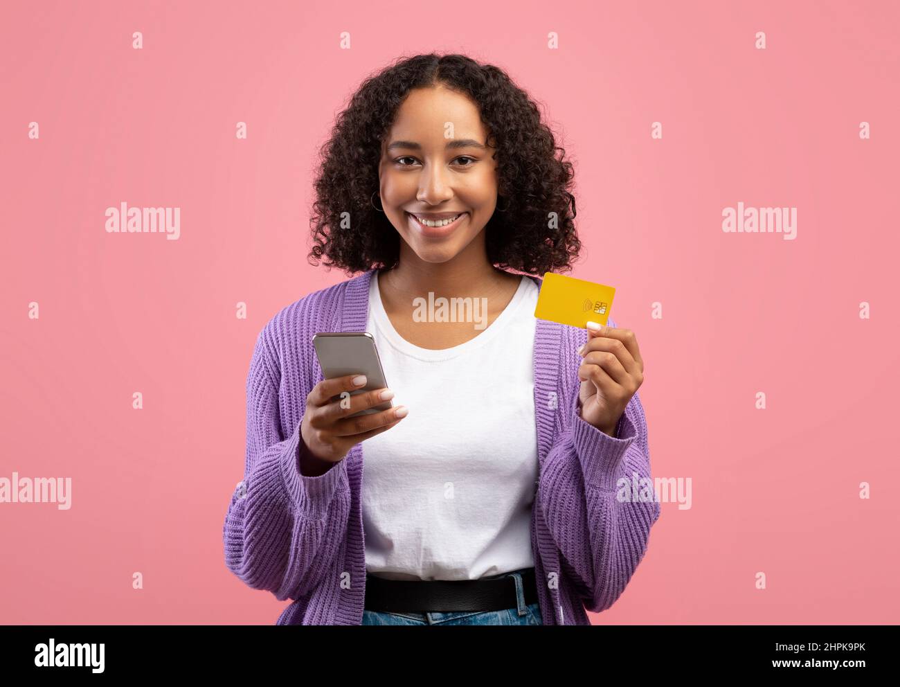 Application d'achat en ligne. Jeune femme afro-américaine souriante utilisant un téléphone portable et une carte de crédit, achetant dans un magasin web Banque D'Images