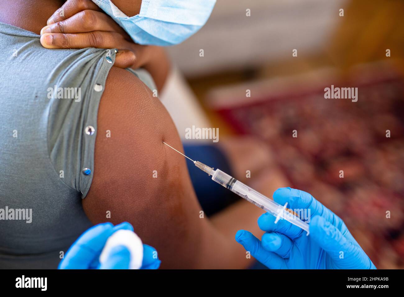 Les mains cultivées d'une femme de race blanche mature médecin vaccinant une fille afro-américaine sur l'épaule Banque D'Images