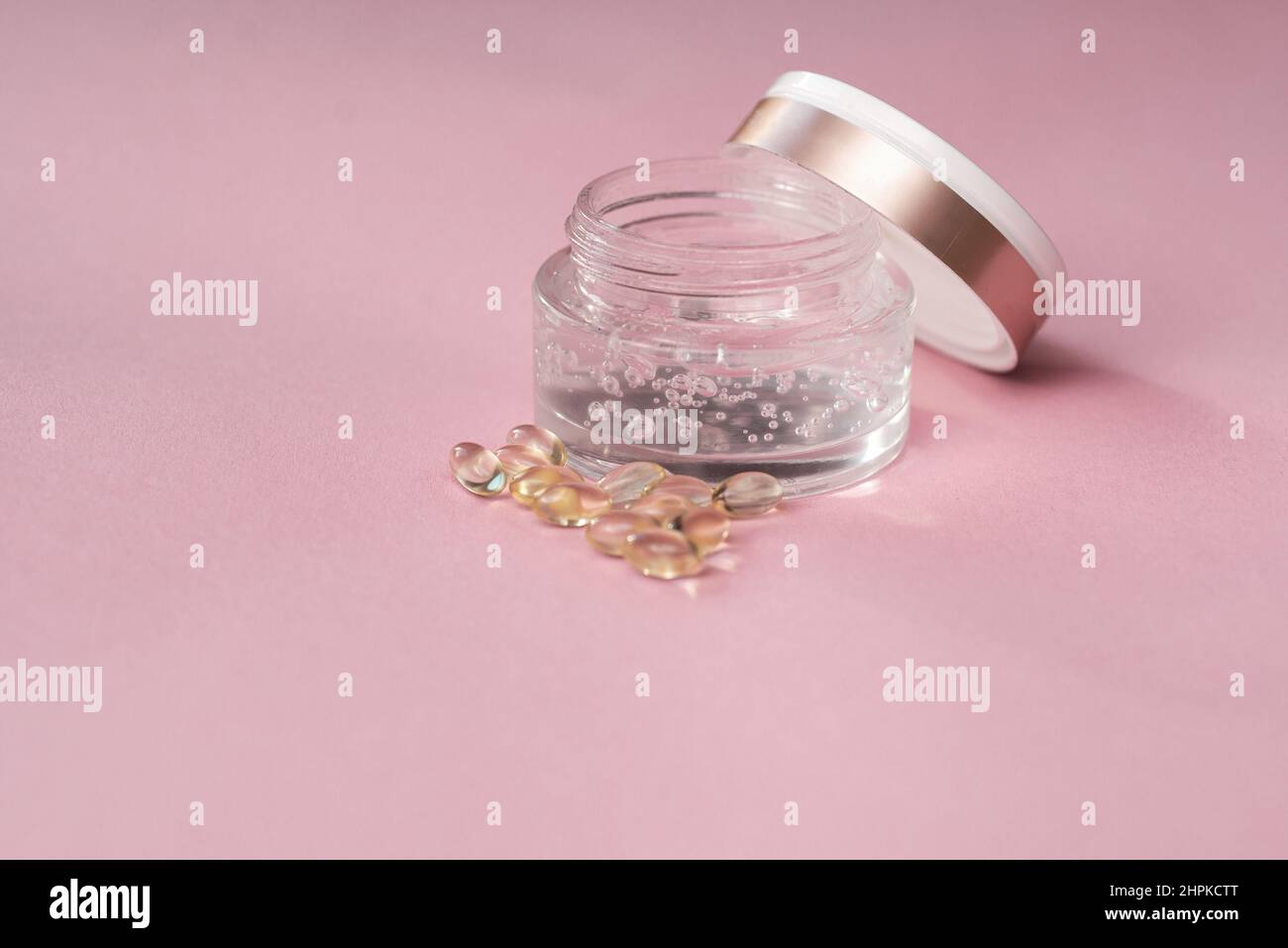 Gélofier avec de l'acide hyaluronique dans un pot en verre et des capsules sur fond rose Banque D'Images
