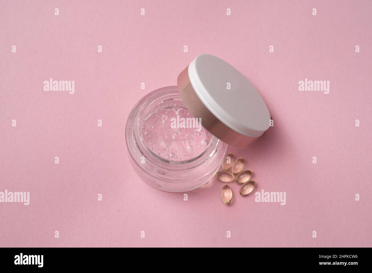 Gélofier avec de l'acide hyaluronique dans un pot en verre et des capsules sur fond rose Banque D'Images