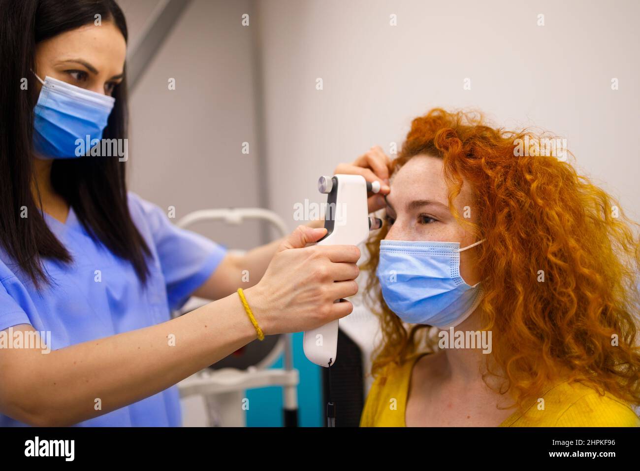 Femme médecin avec un masque de visage examiner les yeux de sa cliente Banque D'Images