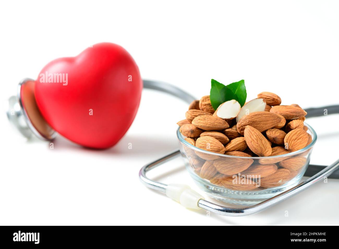 amandes dans une tasse de verre avec stéthoscope et coeur rouge isolé sur blanc. Les amandes contiennent du cholestérol des lipoprotéines de haute densité (HDL) et aident à prévenir Banque D'Images