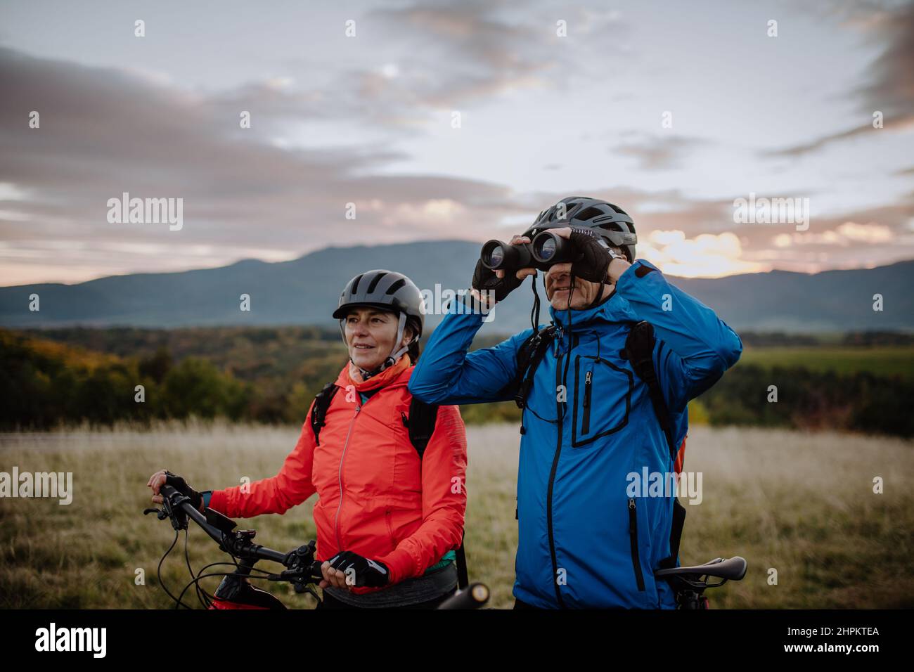 Couple senior motards avec jumelles admirant la nature en plein air dans la prairie en automne. Banque D'Images