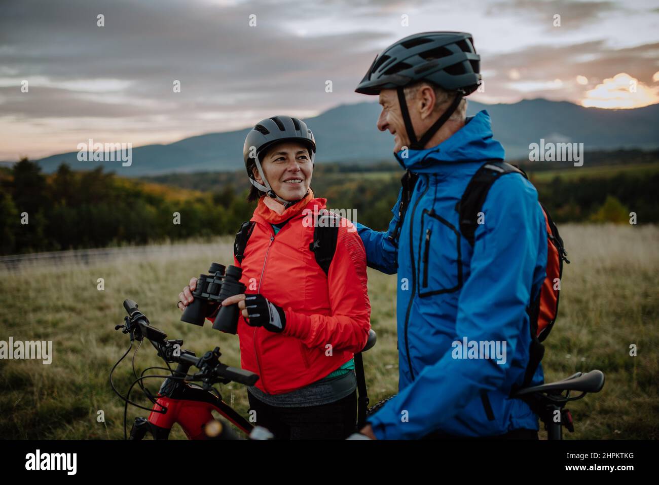Un couple senior de motards avec des jumelles admirant la nature en plein air dans la prairie en automne. Banque D'Images