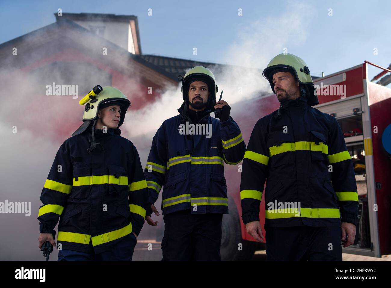 Vue à angle bas de l'équipe de pompiers en action avec la caserne de pompiers et le camion en arrière-plan Banque D'Images