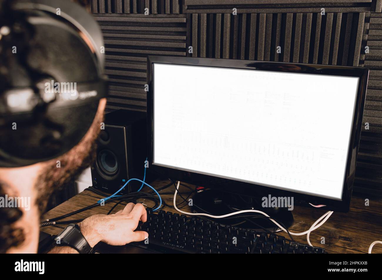 vue arrière d'un jeune caucasien avec un casque utilisant son ordinateur mélangeant et composant de la musique dans son studio à la maison. Banque D'Images