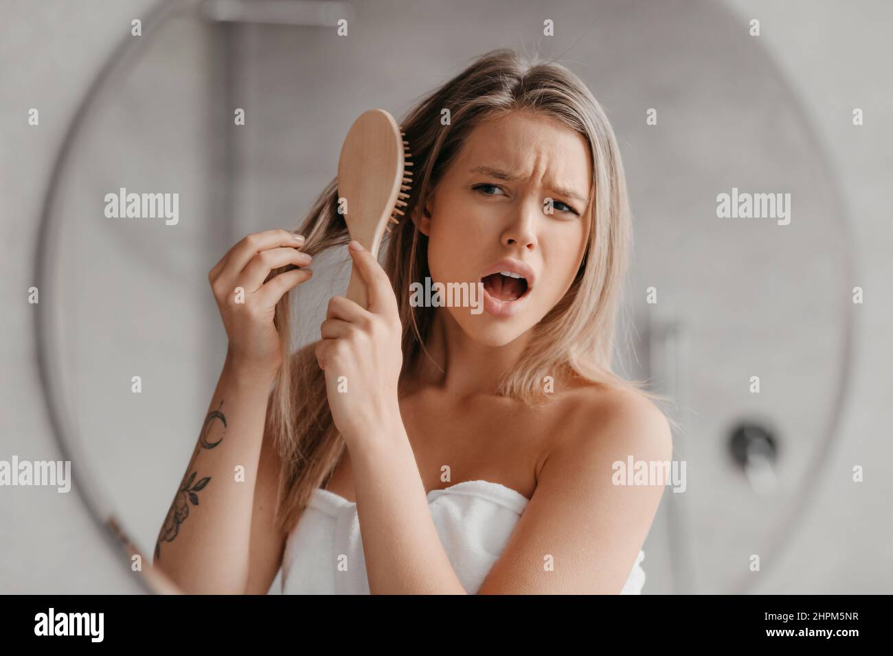 Concept de démêlant les cheveux. Une dame en colère se brossant les cheveux secs avec une brosse à cheveux, souffrant de douleur pendant la routine de beauté Banque D'Images
