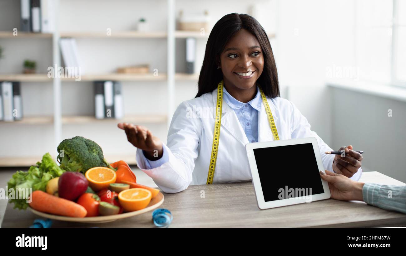 Une diététicienne afro-américaine amicale montrant un plan de régime et recommandant aux patientes de manger des fruits frais Banque D'Images
