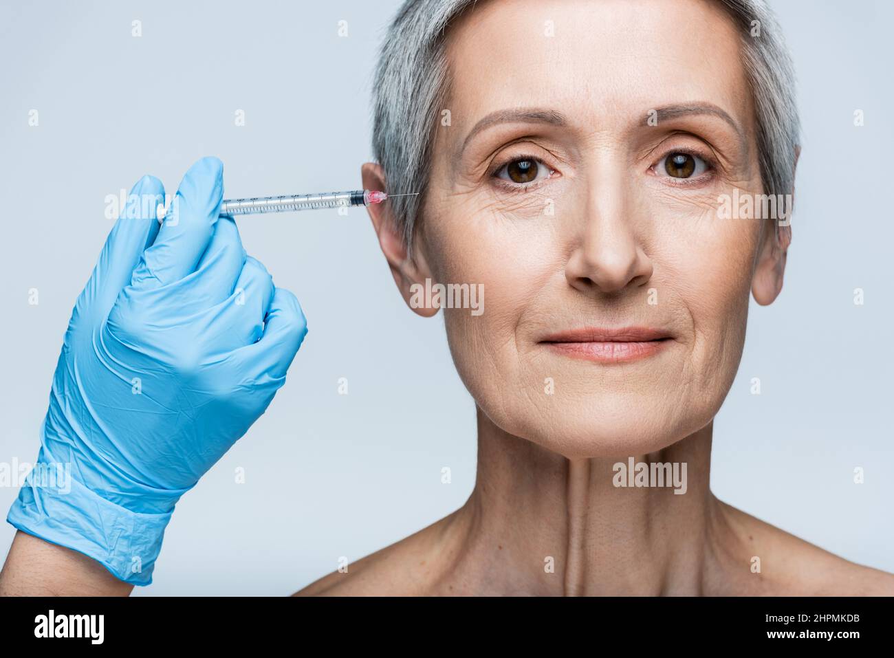 esthéticienne en latex gant tenant la seringue avec injection de beauté près gaie femme mature isolée sur gris Banque D'Images