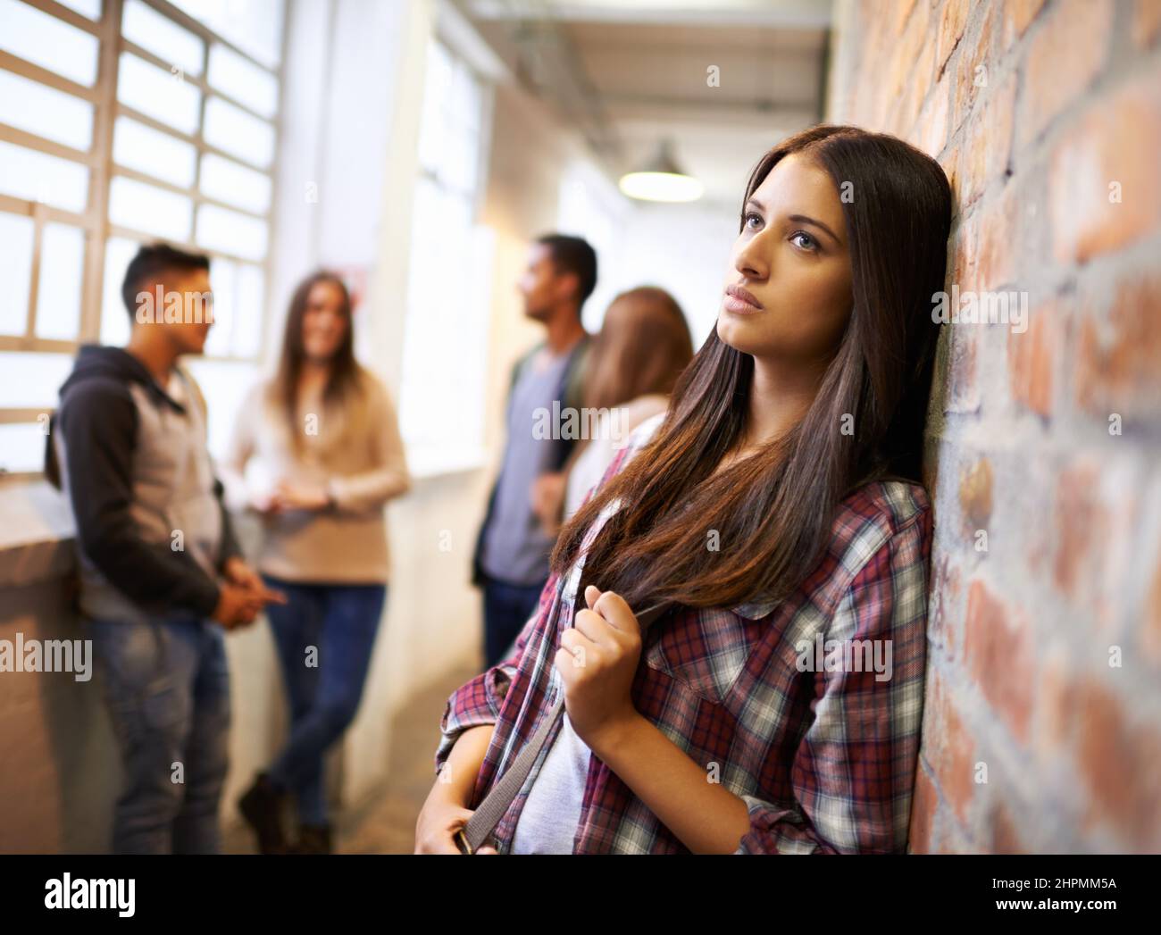 Une vie aimante sur le campus. Photo d'une belle jeune étudiante qui a l'air s'ennuyer tout en se penchant contre un mur de briques sur le campus. Banque D'Images